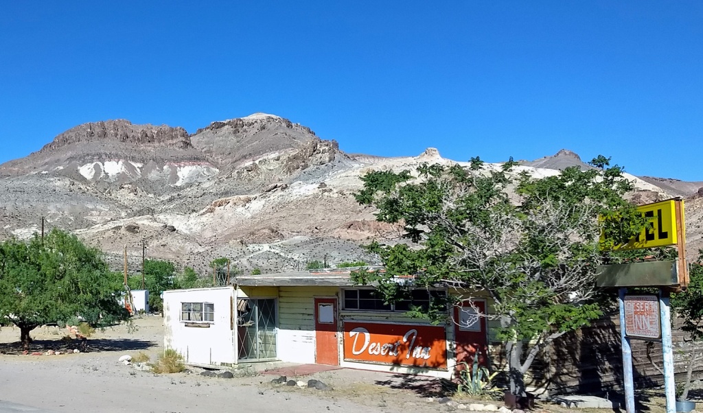 Mountain backdrop for dilapidated roadsie Motel with Desert Inn in white letters on a red board by a red door.